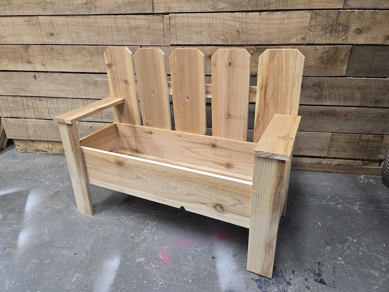 May include: A wooden bench with a planter box built in. The bench has a picket fence style back and is made of natural wood.