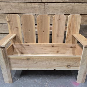 May include: A wooden bench with a planter box built in. The bench is made of natural wood and has a picket fence style back.