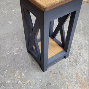 May include: A small, dark blue end table with a wooden top and a lower shelf. The table has an X-shaped design on the sides.