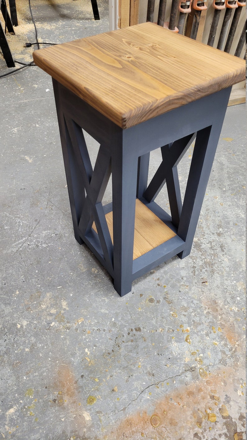 May include: A small, dark blue end table with a wooden top and a lower shelf. The table has an X-shaped design on the sides.