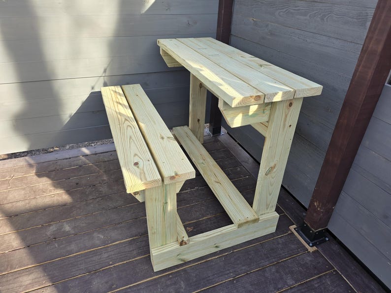 May include: A wooden bench and table set, made of unfinished light wood, with a simple design. The table is attached to a wall and has a bench underneath.
