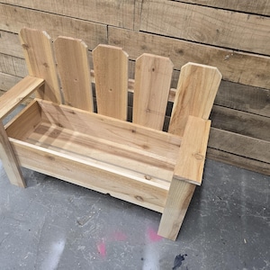 May include: A wooden bench with a planter box built in. The bench is made of natural wood and has a rustic look. The planter box is empty and ready for plants.