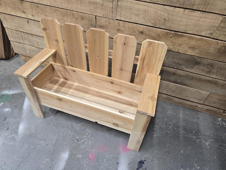 May include: A wooden bench with a planter box built in. The bench is made of natural wood and has a rustic look. The planter box is empty and ready for plants.