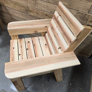 May include: A wooden chair with a slatted back and seat, and a wide armrest on one side. The chair is made of natural wood with a light brown finish.