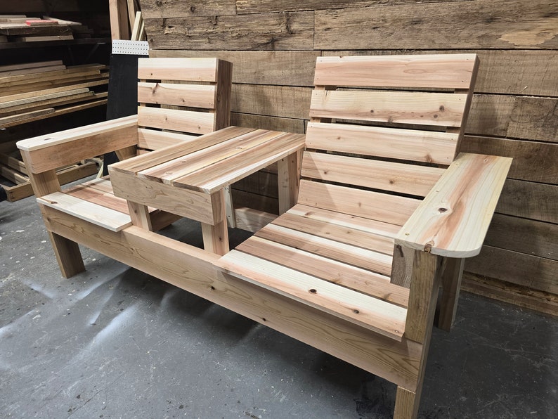 Pu&ograve; includere: Una panca in legno con due posti a sedere e un tavolino al centro. La panca &egrave; realizzata con assi di legno naturale e ha un aspetto rustico.