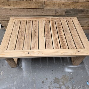 May include: A rectangular wooden coffee table with a slatted top and a natural wood finish. The table has a simple, modern design and is perfect for any living room or outdoor space.