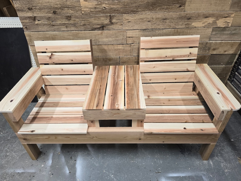 Pu&ograve; includere: Una panca in legno con due posti a sedere e un tavolino al centro. La panca &egrave; realizzata in legno naturale con una finitura marrone chiaro. Il tavolino &egrave; anch'esso in legno e ha una finitura in legno naturale.
