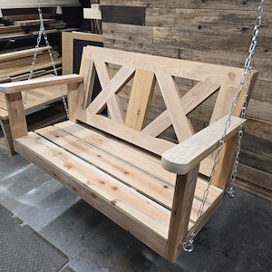 May include: A wooden swing bench with a slatted seat and a decorative X-shaped back. The swing is hanging from two chains.