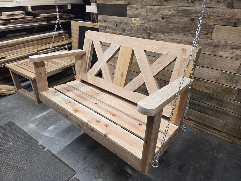 May include: A wooden swing bench with a slatted seat and a decorative X-shaped back. The swing is hanging from two chains.