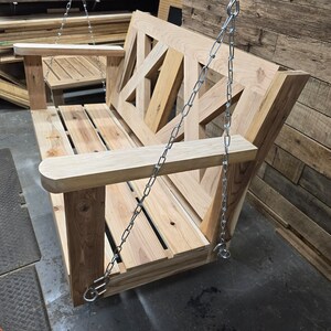 May include: A wooden swing bench with a geometric design on the back. The swing is suspended by two silver chains.