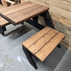 May include: A wooden picnic table with two benches. The table and benches are stained a dark brown color. The table has a black metal frame. The benches are attached to the table and have black metal legs.