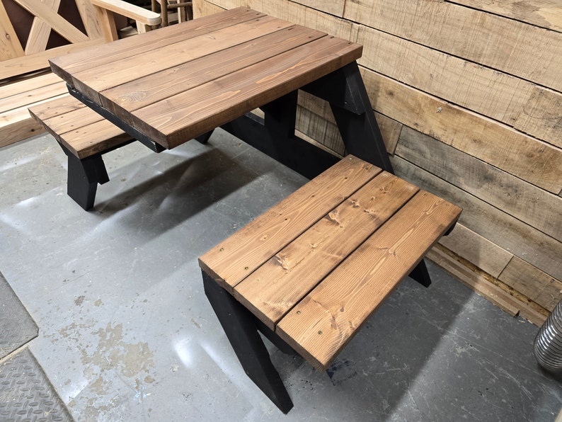 May include: A wooden picnic table with two benches. The table and benches are stained a dark brown color. The table has a black metal frame. The benches are attached to the table and have black metal legs.