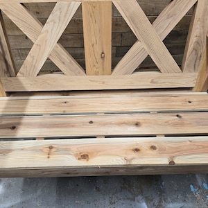 May include: A wooden swing with a slatted seat and a criss-cross design on the back. The swing is made of natural wood and has a rustic look.