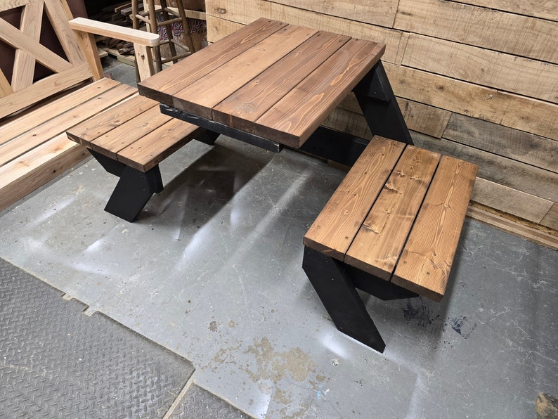 May include: A wooden picnic table with two benches. The table and benches are made of brown wood with black metal legs. The table is square and the benches are rectangular.