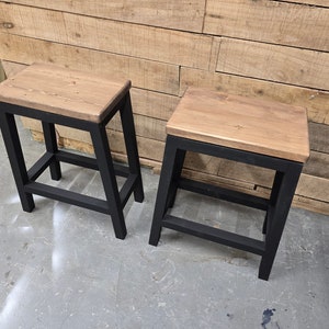 Peut inclure: Deux tabourets en bois avec des cadres en métal noir. Les tabourets ont un design simple et sont parfaits pour ajouter une touche de charme rustique à n'importe quel espace.