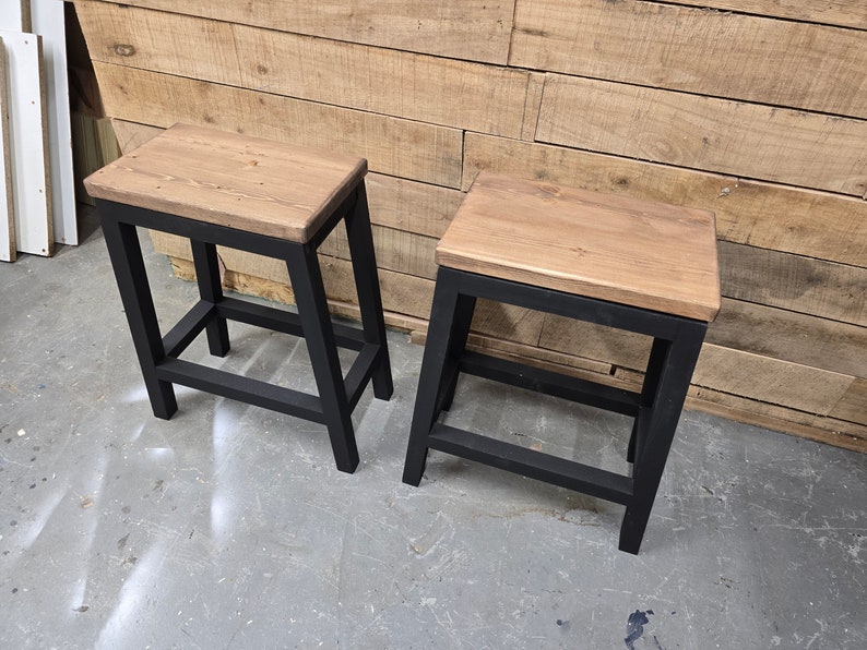 Puede incluir: Dos taburetes de madera con marcos de metal negro. Los taburetes tienen un dise&ntilde;o sencillo y son perfectos para a&ntilde;adir un toque de encanto r&uacute;stico a cualquier espacio.