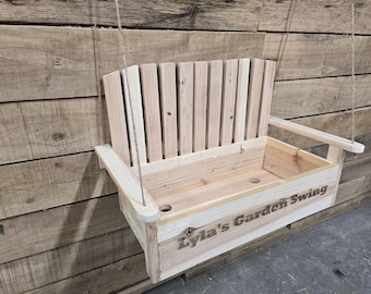 May include: A wooden garden swing with a slatted back and a personalized inscription that reads "Lyla's Garden Swing".