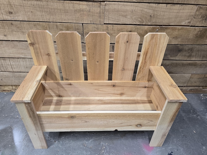 May include: A wooden bench with a planter box built in. The bench has a picket fence design on the back and is made of natural wood.