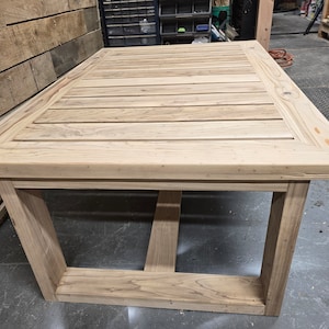 May include: A light wood table with a slatted top and a simple, rectangular frame. The table is made of unfinished wood and has a natural, rustic look.