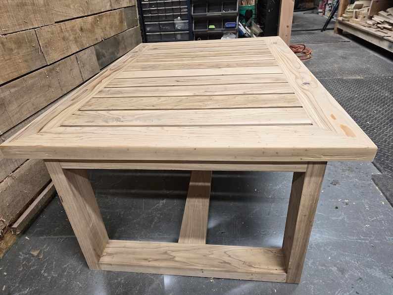 May include: A light wood table with a slatted top and a simple, rectangular frame. The table is made of unfinished wood and has a natural, rustic look.