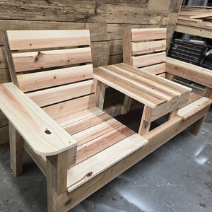Pu&ograve; includere: Una panca in legno con un tavolo integrato al centro. La panca &egrave; realizzata con assi di legno naturale e ha un aspetto rustico.