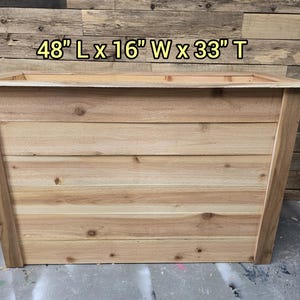 May include: A wooden planter box with a natural wood finish. The planter is 48 inches long, 16 inches wide, and 33 inches tall.  The planter is made of cedar wood and has a natural wood grain.