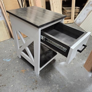May include: A white and black end table with a drawer that is open. The drawer has a black interior and a black metal slide. The table has a black top and a white base with an X-shaped design.