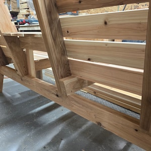 Pu&ograve; includere: Una panca in legno con schienale a doghe e una seduta larga. La panca &egrave; realizzata in legno naturale e ha un aspetto rustico.