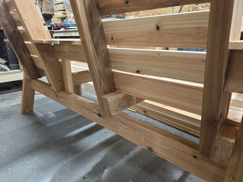 Pu&ograve; includere: Una panca in legno con schienale a doghe e una seduta larga. La panca &egrave; realizzata in legno naturale e ha un aspetto rustico.