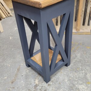 May include: A small, dark blue end table with a wooden top and a shelf. The table has an X-shaped design on the front and sides.