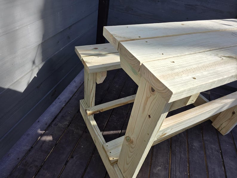 May include: A wooden picnic table with a bench attached to one side. The table and bench are made of unfinished light brown wood.