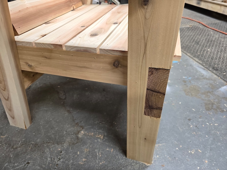 May include: Close-up of a wooden chair with a natural finish. The chair has a simple design with a wide seat and a sturdy frame. The chair is made of solid wood and has a rustic look.
