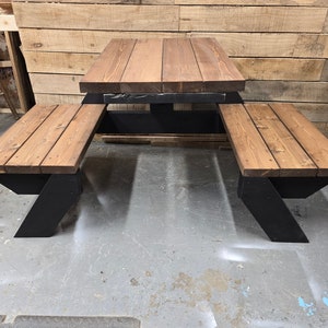 May include: A wooden picnic table with two benches. The table and benches are made of brown wood with black metal legs. The table is square and the benches are rectangular.