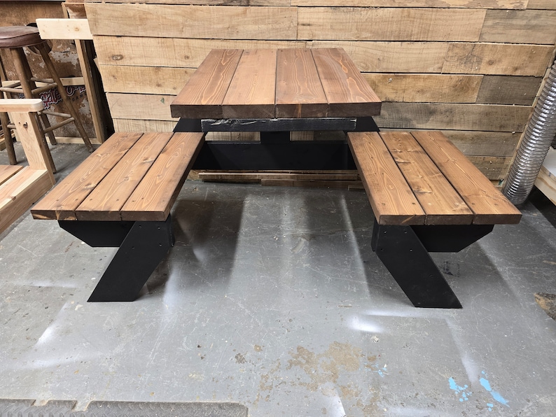 May include: A wooden picnic table with two benches. The table and benches are made of brown wood with black metal legs. The table is square and the benches are rectangular.