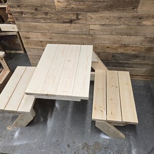 May include: A wooden picnic table set with a rectangular table top and two benches. The table and benches are made of unfinished light wood.