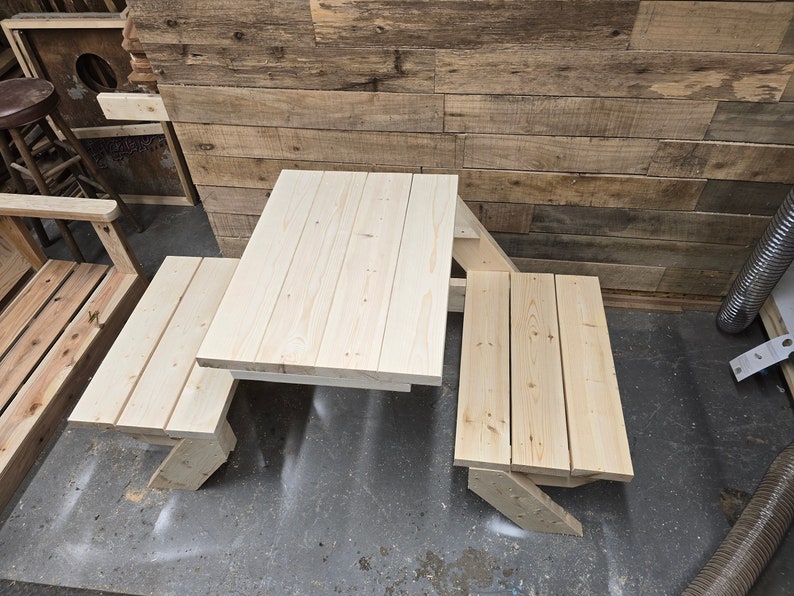 May include: A wooden picnic table set with a rectangular table top and two benches. The table and benches are made of unfinished light wood.
