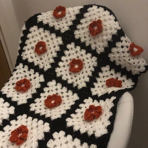 May include: A crocheted blanket with a black and white checkered pattern and orange flowers.