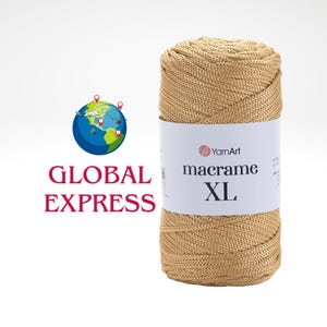 Puede incluir: Un carrete de hilo macramé XL de color dorado con una etiqueta blanca con el logotipo de YarnArt. Las palabras "macrame XL" están impresas en la etiqueta. Un globo terráqueo con las palabras "GLOBAL EXPRESS" está a la izquierda.