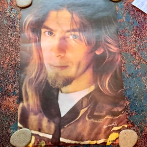 May include: A vintage poster featuring a close-up portrait of a man with long, wavy hair. He is wearing a brown leather jacket and has a beard. The poster is signed "Clay  Mays" in the bottom right corner.