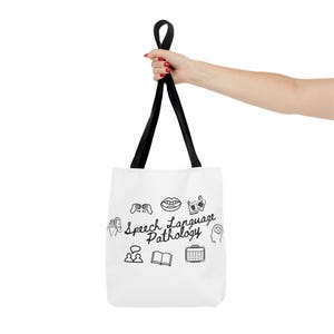 Puede incluir: Bolso tote blanco con asas negras. La bolsa presenta las palabras "Speech Language Pathology" e iconos relacionados. La bolsa está sostenida por una persona. La bolsa está hecha de un material resistente.