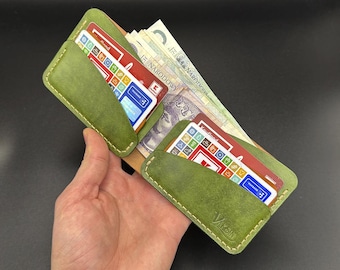 Op de afbeelding: Een groene leren portemonnee met twee kaartsleuven en een geldclip. De portemonnee is open en bevat verschillende kaarten en biljetten.