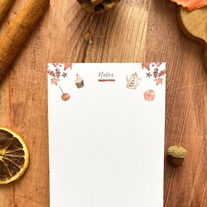 Peut inclure: Un bloc-notes vierge avec des illustrations à l'aquarelle d'éléments d'automne, dont des feuilles, des champignons et une théière. Le mot "Notes" est en haut. Le bloc-notes est sur une surface en bois avec des éléments décoratifs.