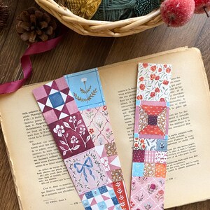 Peut inclure: Deux marque-pages décoratifs avec des motifs floraux et géométriques. L'un présente un motif patchwork avec un nœud, des fleurs et des formes géométriques dans des tons de rose, de bleu et de bordeaux. L'autre a un motif floral rouge et blanc.