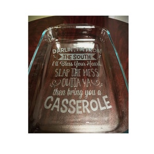 May include: A rectangular clear glass baking dish featuring etched white text that reads: DARLIN', I'M FROM THE SOUTH, I'll Bless Your Heart, SLAP THE MESS OUTTA YA, then bring you a CASSEROLE. The dish has integrated handles on the short ends.