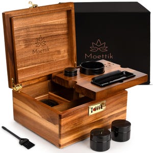 May include: A wooden box with the brand name "Moettik" engraved on the lid. The box is open, revealing compartments and accessories, including black containers and a brush. The box has a combination lock.