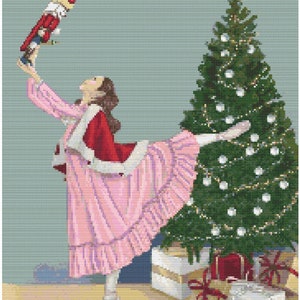May include: A ballerina wearing a pink dress and red bodice holds a toy nutcracker above her head. She is standing in front of a decorated Christmas tree with presents underneath.