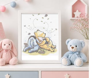 May include: A framed wall art print featuring a watercolor illustration of a yellow bear and a blue donkey sitting together on green grass. The bear is holding a small black pot, and there are swirling leaves in the air above them.