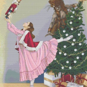 May include: A young ballerina in a pink dress and red cape holds a nutcracker doll while standing near a decorated Christmas tree with presents underneath.