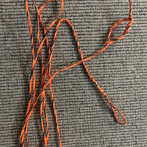 May include: A black and orange bowstring for archery. The string is coiled and ready to be used.