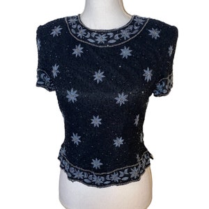 May include: A black sequined top with a silver floral design. The top has short sleeves and a round neckline.